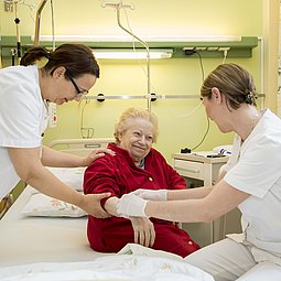 Eine ältere Dame wird von zwei Krankenpflegerinnen betreut